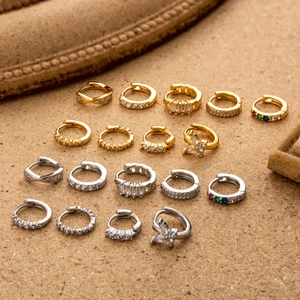 Set of 16 gold and silver copper hoop earrings with zircon stones on stone surface