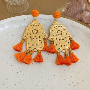 Detailed close-up of golden Hamsa hand earrings with vibrant orange tassels and weaving