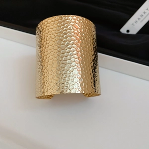 Macro detail of the wide gold hammered metal cuff bracelet showing textured surface