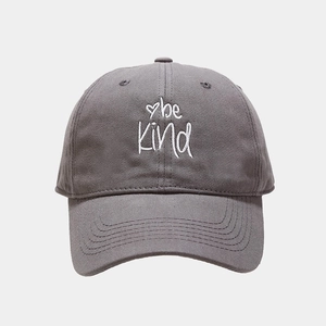 Detail of white be kind embroidery on dark grey cotton baseball cap with heart pattern