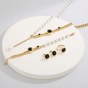 Detailed view of golden jewelry set with pearls and black stones on white display tray