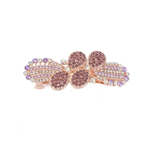 Detail of rose gold alloy bow hair clip with purple and white rhinestones on white background