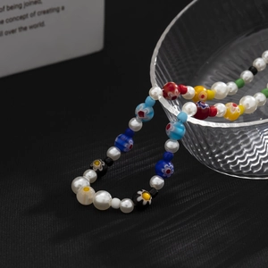 Handmade necklace with white pearls and colorful glass flower beads on a dark background