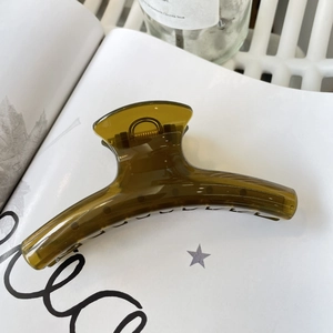 Detail of a large olive green transparent hair claw clip with golden metal spring on a magazine
