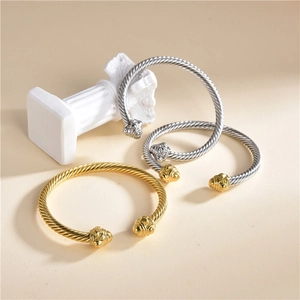 Detail of twisted cable wire cuff bracelets in gold and silver finish on stone pillar