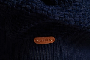 Macro view of navy knit cardigan texture and brown leather label on the sleeve