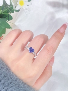 Detail of a heart-cut blue gemstone ring featuring side heart accents on a silver band