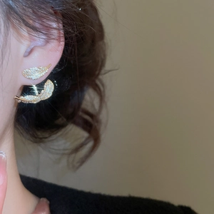 Model wearing gold leaf drop earrings with sparkling cubic zirconia on a warm background