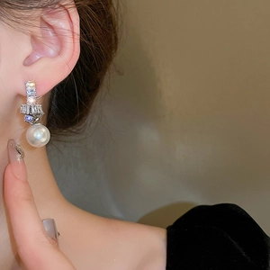 Close-up of model wearing silver knot earrings with sparkling zircon and pearl pendant
