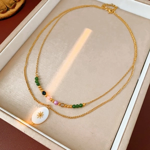 Detail of vintage gold layered necklace with colorful beads and white sunburst oval pendant