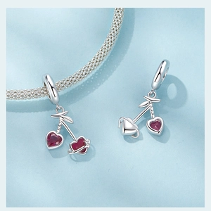 Detail of a cherry pendant charm with heart-shaped red gems on a braided silver bracelet