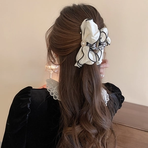 Detail of a large fabric bow hair claw clip with pearl center and black trim on dark hair