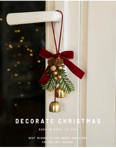Detail of red velvet bow with golden bells and pine cone on white door handle