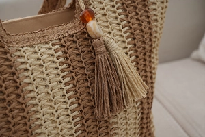 Detailed macro view of striped straw tote with hanging brown tassels and decorative wood beads