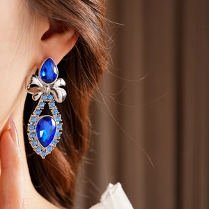 Close-up of vintage silver bow earrings with large blue teardrop crystals on a model