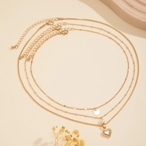 Close-up of layered gold necklace with heart pendant, imitation pearls and metal sequins