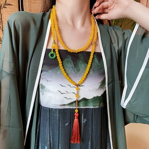 Long collier de perles avec un gland rouge et un anneau vert porté par un mannequin femme