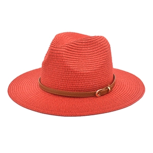 Close-up of red straw fedora hat featuring a brown leather band and golden buckle detail