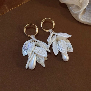 Detailed close-up of golden leaf earrings with drop pearls on brown leather background