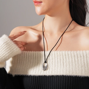 Silver irregular oval pendant on black cord shown on model neck with knit sweater