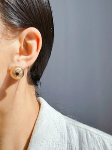 Detail of vintage gold sunburst stud earrings with red ruby-style zircon on model