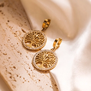 Golden Tree of Life earrings with cubic zirconia stones on a beige stone and silk background