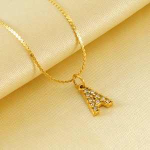 Collana con lettera A in acciaio dorato e diamanti su elegante sfondo in seta gialla