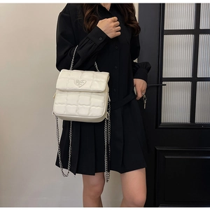 Detail of white quilted crossbody bag with silver chain and heart-shaped logo plate