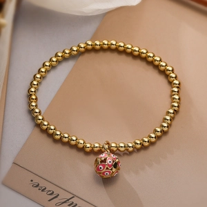 Gold beaded bracelet featuring a pink enamel evil eye hollow charm on a warm background
