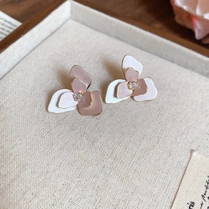 Elegant pink and white floral stud earrings with pearl and crystal detail on fabric background