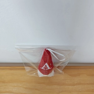 Macro shot of red knitted gnome ornament with white embroidered letter A in plastic bag