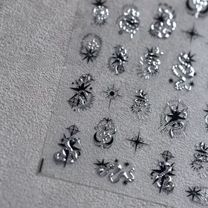 Close-up of 3D silver nail stickers with mystical snake, moon and star metallic patterns