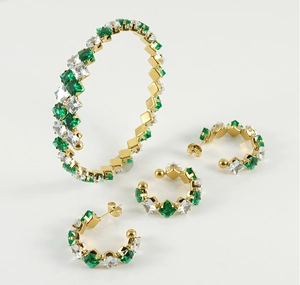 Detail of gold jewelry set with emerald-cut green gemstones and earrings on white background