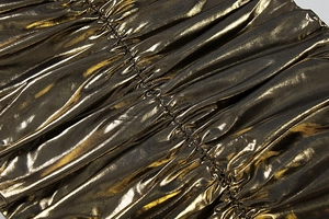 Détail macro du tissu plissé doré métallisé avec texture réfléchissante et couture centrale