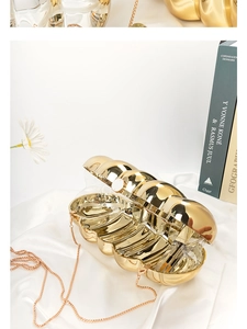 Detail shot of golden shell-shaped evening clutch with ripple texture on white silk fabric