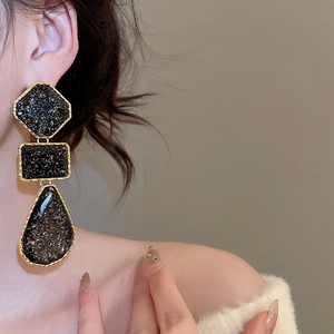Close-up of geometric black resin drop earrings with gold edges on a female model