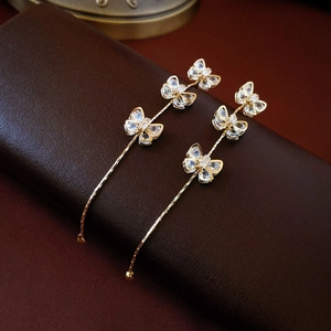 Detailed close-up of gold bow tassel earrings with sparkling zircon on leather texture