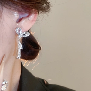 Close-up of sparkling zircon bow earrings with dangling ribbon tassels on model's ear