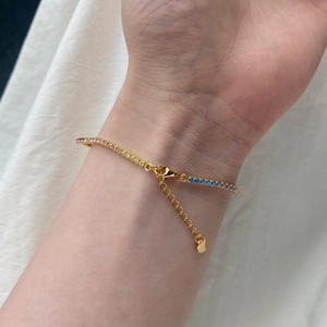Detailed view of gold plated tennis bracelet with colorful gemstones and heart charm