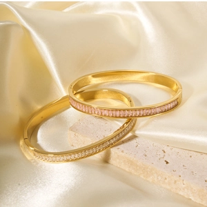 Detail shot of gold baguette-cut zircon bracelets on cream satin and travertine stone