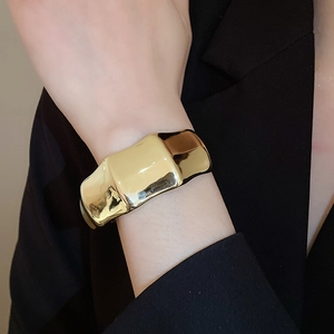 Close-up of a wide chunky gold oval acrylic open cuff bracelet on a model wrist