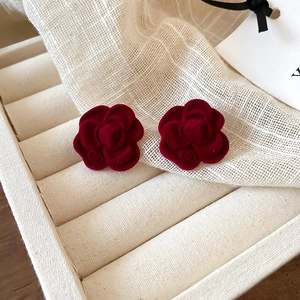 Detail view of elegant dark red flocked camellia stud earrings on a jewelry tray