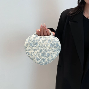 Close-up of blue floral quilted heart shaped cotton makeup bag held by a model