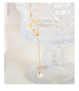 Detail of rose gold tulip necklace with white shell flower and dangling pearl on glass
