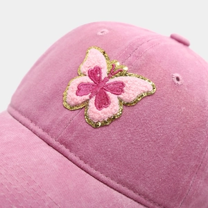 Détail macro d'une broderie papillon sur une casquette de baseball en velours rose