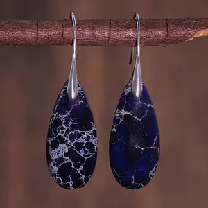 Detail of teardrop blue imperial stone earrings hanging on a natural wooden branch