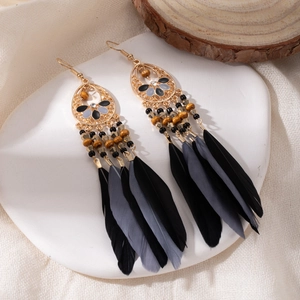 Detail of bohemian long fringe earrings with black and gray feathers on white ceramic