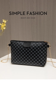 Close-up of black crossbody bag with clover pattern, zipper closure and gold chain strap