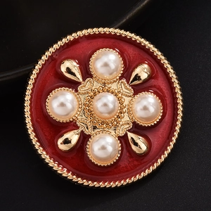 Macro detail of a red enamel brooch with gold rope edge and pearl cross setting