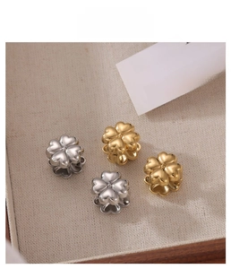 Macro shot of gold and silver four-leaf clover earrings on a textured fabric backdrop